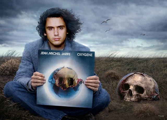 Junger Jean Michel Jarre hält das Album Oxygene in einer windigen Landschaft, daneben ein halb versunkener Totenschädel als surrealer Bezug zum Albumcover.
