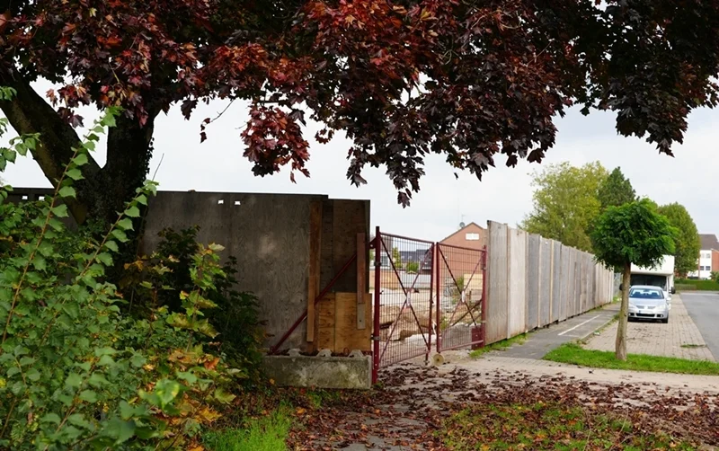 Ein langer Bauzaun mit großer Holzwand trennt das neue Schulgelände der Petrus-Canisius Grundschule vom Gehweg in Weeze.