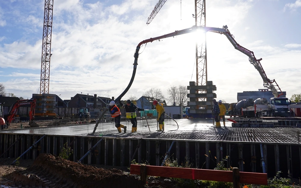 Arbeiter betonieren die Bodenplatte der neuen Petrus-Canisius-Grundschule in Weeze. Im Hintergrund stehen zwei große Baukräne und eine Betonpumpe.