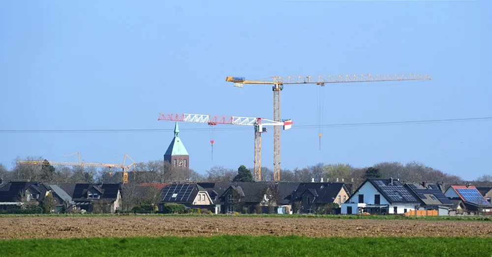 Blick über Weeze mit mehreren Baukränen der neuen Petrus-Canisius-Grundschule und dem Kirchturm im Hintergrund.