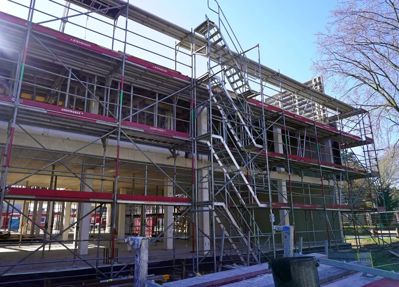 Seitenansicht der neuen Petrus-Canisius-Grundschule in Weeze mit großem Baugerüst und Außentreppe.