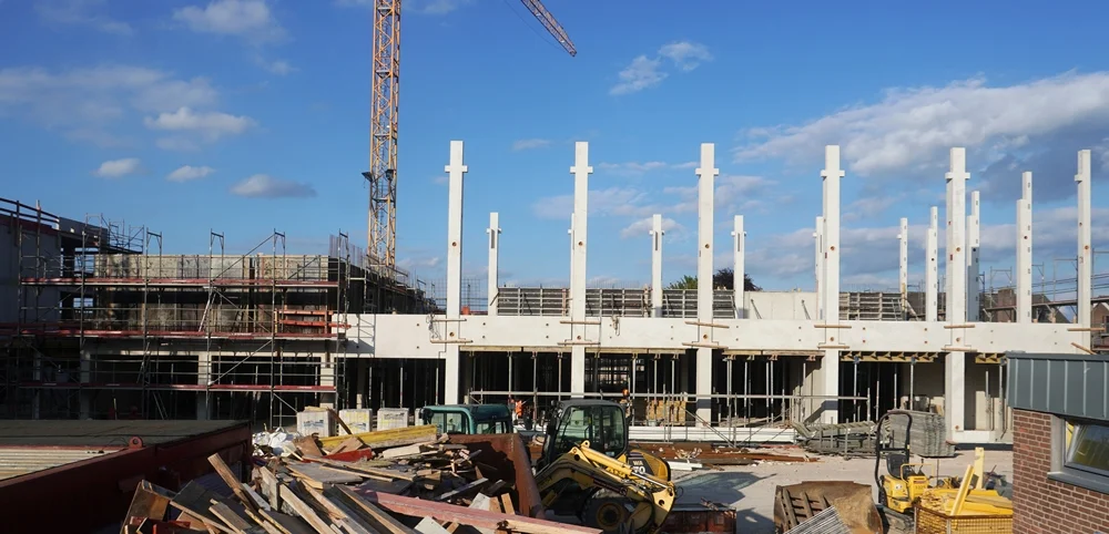 Mit dem Stick fotografierte Ansicht des Schulneubaus in Weeze. Zahlreiche weiße Betonstützen, Baugeräte und Materialien prägen die Baustelle unter einem freundlichen Himmel mit Wolken.