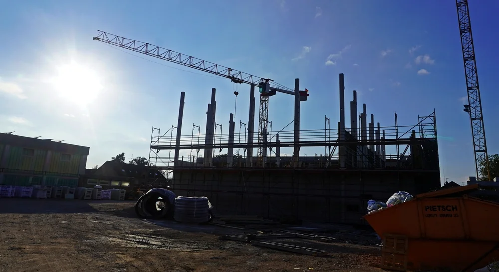 Abendstimmung auf der Schulbaustelle in Weeze. Die tief stehende Sonne taucht Kräne, Gerüste und Betonstützen in kräftiges Gegenlicht und lässt die Konturen des wachsenden Schulgebäudes eindrucksvoll hervortreten.