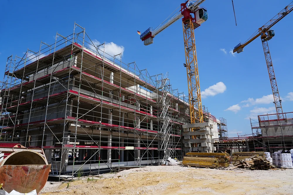 Rohbau der neuen Grundschule in Weeze mit eingerüsteter Fassade und zwei Baukränen während der Bauarbeiten im Juli 2026.