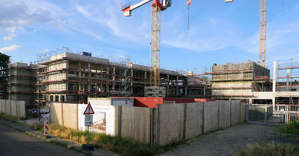 Gesamtansicht der Baustelle der neuen Petrus-Canisius-Grundschule in Weeze Anfang August 2026 mit Baukränen, Gerüsten und dem Rohbau im Abendlicht.