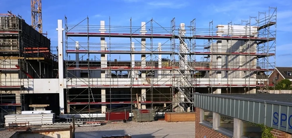 Rohbau der neuen Petrus-Canisius-Grundschule in Weeze mit Betonstützen, Gerüsten und der alten Sporthalle im Vordergrund rechts.